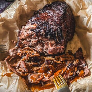 Fertig gegrilltes Pulled Pork mit Raucharoma auf Butterbrotpapier, Fleisch mit Gabeln zerteilt.