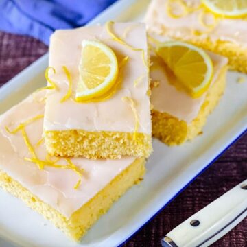 Zitronenkuchen mit Frischkäseglasur, in Portionen geschnitten und mit Zitronenscheiben garniert auf weißem Tablett.